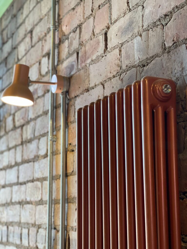 A vertical copper radiator sits against a brick wall